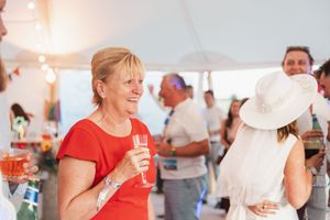 Wedding guests enjoying drinks and conversation under a white tent with festive decorations.