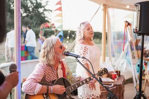 Musicians perform on stage under a tent outdoors during a festival with colorful decorations.