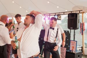Party guests dancing and socializing at a formal event under white tent with sound equipment.