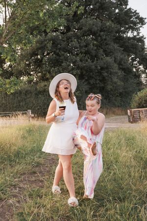 Two people in white summer outfits sharing a lighthearted moment in a grassy field at sunset.
