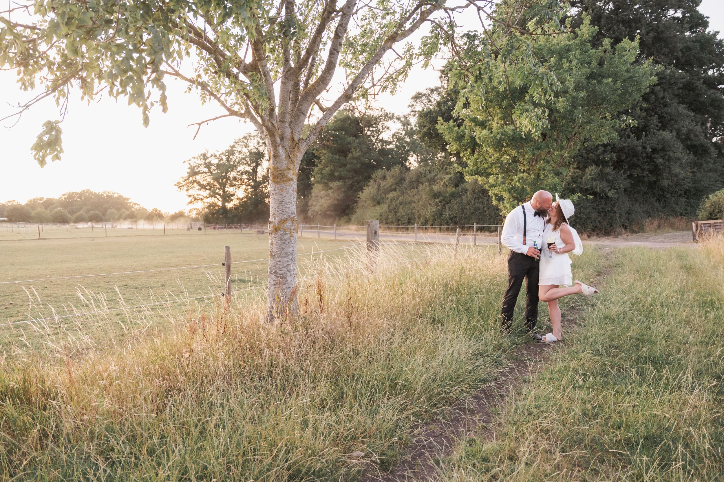 Couple walking through a golden field at sunset with tall grass and trees in the background.