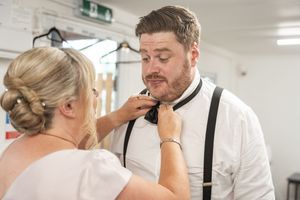 Final adjustments being made to formal wedding attire in a bright dressing room.