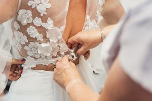 Close-up of delicate lace detail and buttons on the back of a wedding dress being fastened.
