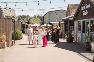 People walking along rustic shopping area with hanging string lights and wooden buildings.