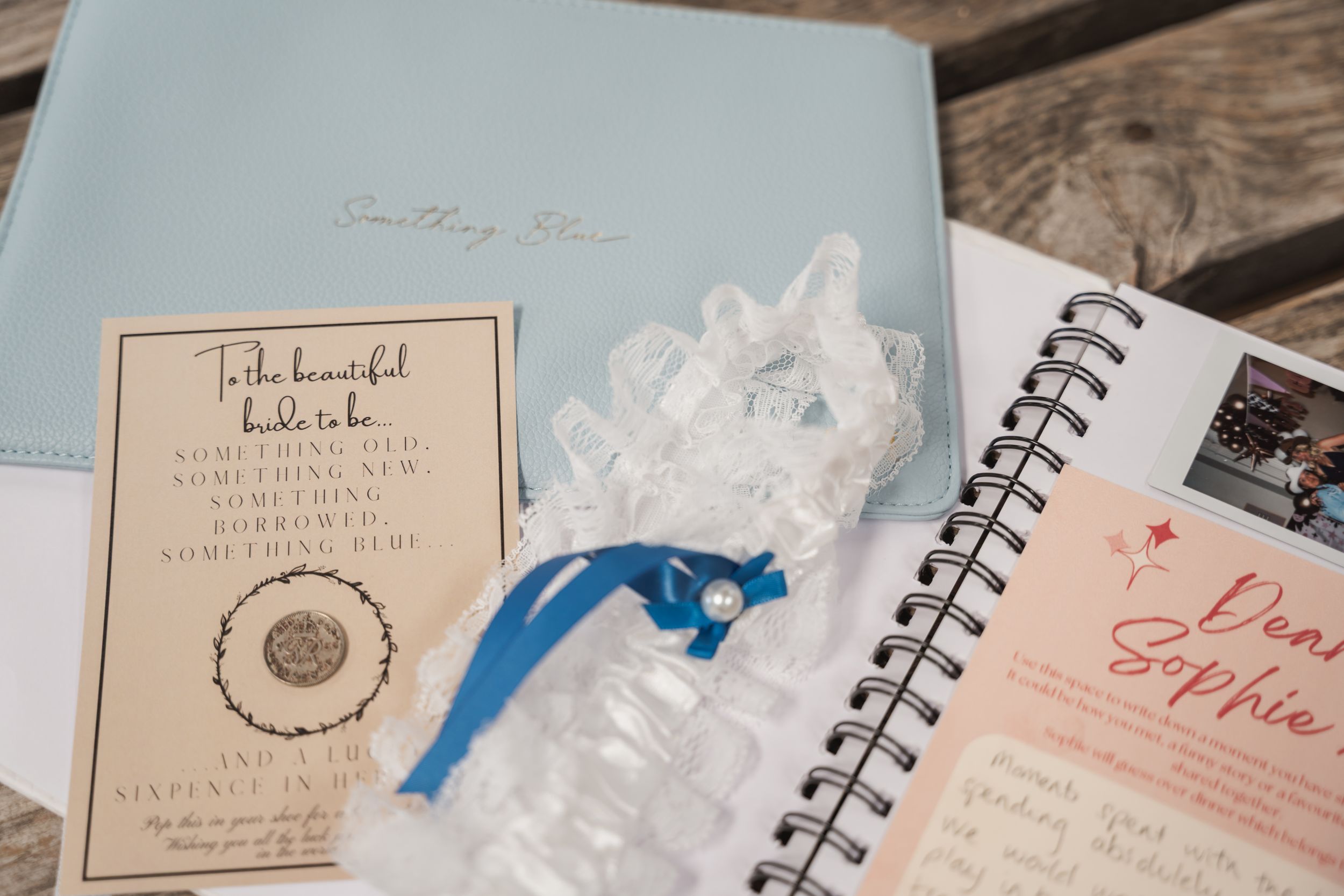 Wedding details including a garter, invitation and planning notebook laid out on wooden surface.