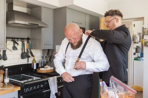 Getting ready scene with formal attire being adjusted in a modern kitchen setting.