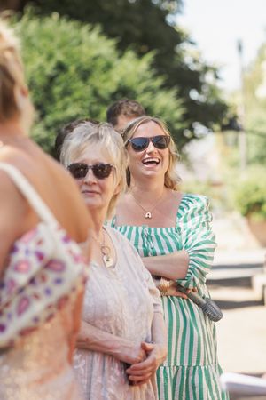 Candid outdoor shot of people laughing and hugging, with one wearing green stripes and another in light pink.