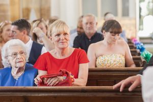 Wedding guests seated in church pews watching ceremony with colorful floral decorations.