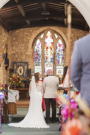 View of a church interior with stained glass windows and floral decorations during a wedding ceremony.