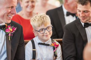 Young attendee in glasses and bow tie smiling during a formal wedding ceremony.
