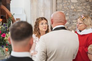 A wedding ceremony takes place in a stone church with floral decorations and gathered guests.