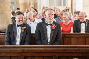 People seated in wooden church pews laugh together during a joyful moment.