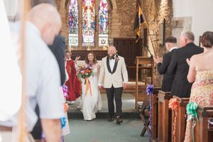 A wedding ceremony taking place inside a church with stained glass windows and orange floral decorations.