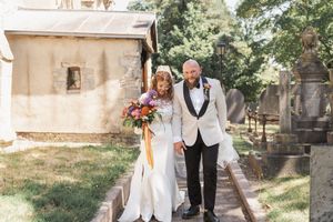 Wedding ceremony held outside stone church with guests seated in wooden chairs.