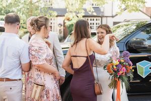 Guests chat outside at a casual outdoor event while holding colorful floral bouquets and beverages.