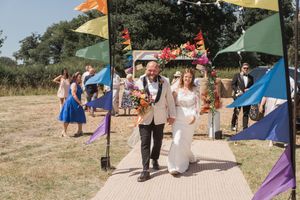 Celebratory outdoor wedding processional with colorful flags lining the path.