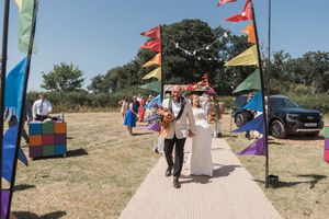 A couple walks down a decorated path with colorful flags and banners at an outdoor celebration.