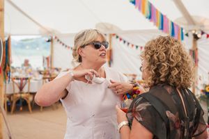 Two guests having an animated conversation at a wedding reception under a tent with colorful bunting decorations.