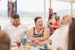 Party guests laughing together at a festive celebration under a tent with colorful decorations.