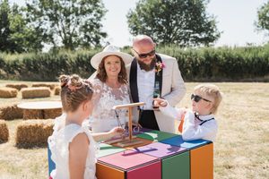 Children and adults play educational games at tables set up in a sunny outdoor field with hay bales.