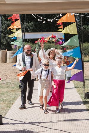 A wedding celebration with people walking under colorful triangle bunting flags on an outdoor path during a sunny day.