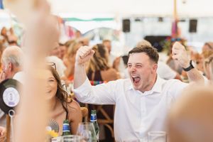 An energetic celebration moment captured under a party tent with raised hands and excitement.