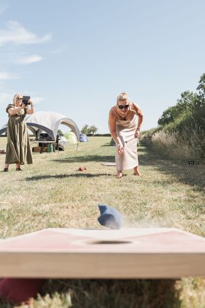 People playing outdoor lawn games on a grassy hillside under blue summer skies.