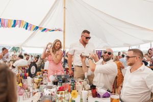 Wedding guests gathered under a white tent enjoying drinks and festivities at a celebration.