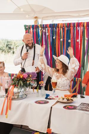 Festive party scene with colorful ribbon streamers and people celebrating at tables under a white tent.
