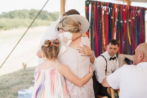 Emotional moment at an outdoor wedding celebration under white tent with colorful decorative ribbons.