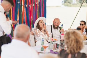 Guests enjoying a celebration under a tent with colorful streamers decorating the space.
