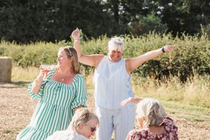 People dancing and celebrating outdoors on a sunny day with green foliage in background.