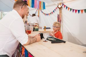 Child engaging with guest at festive party booth decorated with colorful bunting.