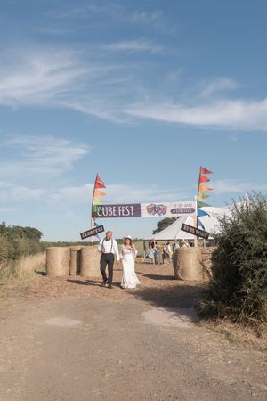 Couple walks toward festival entrance with colorful flags under blue summer sky.