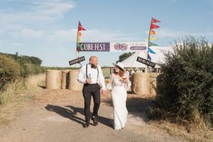 A couple walks together down a rustic dirt path decorated with colorful festival flags and hay bales.