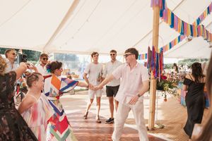Lively wedding reception under a tent with colorful bunting and guests dancing on wooden floor.