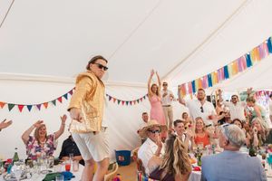 Festive celebration under white tent with guests dancing and colorful bunting decorations.