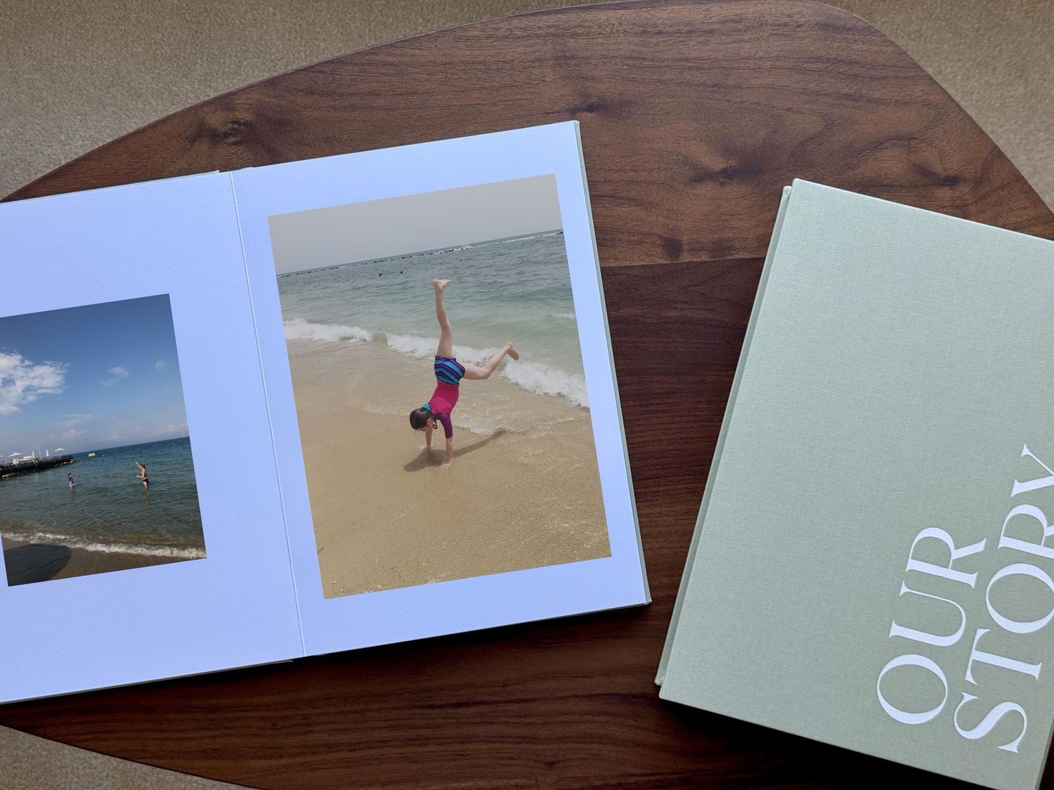 Photo album and book titled 'OUR STORY' on wooden table surface showing beach photography inside.