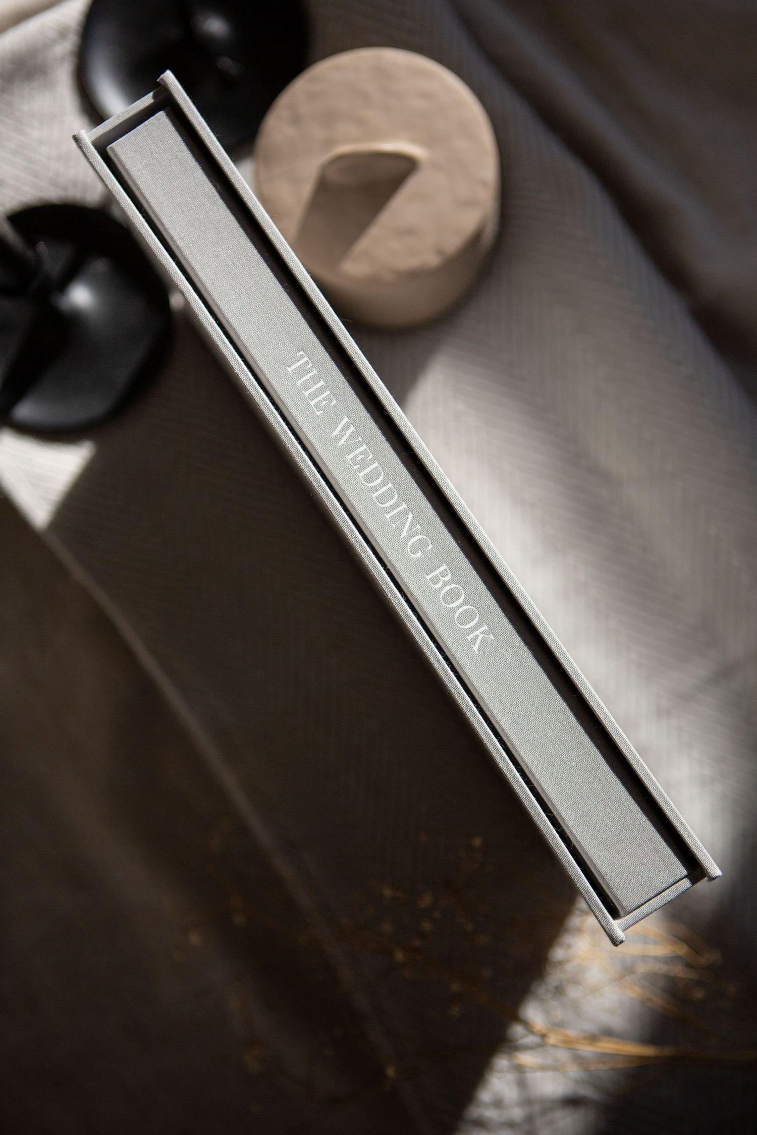 Gray hardcover book spine photographed on dark surface with dramatic lighting and shadows.