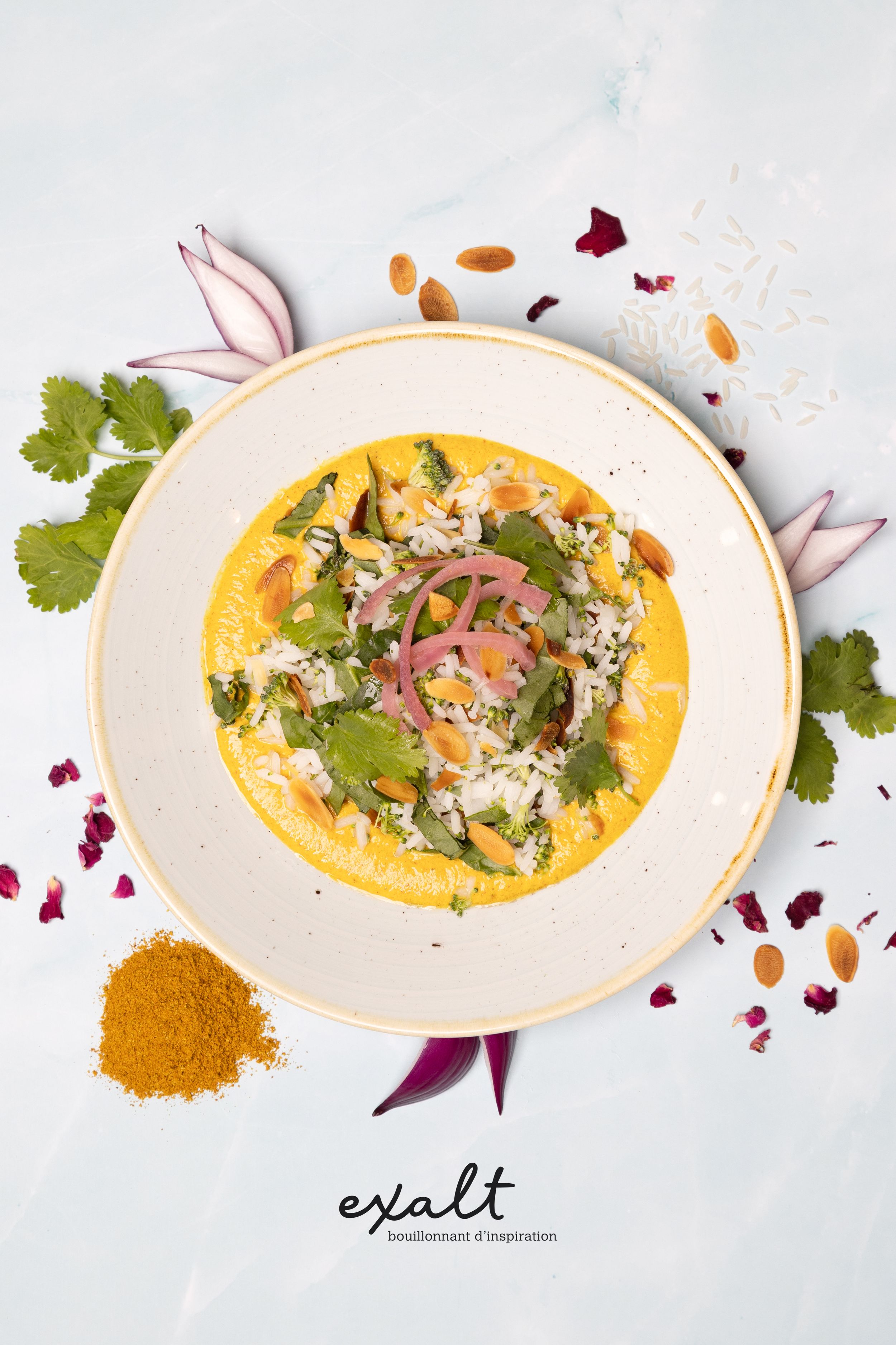 Colorful curry dish garnished with herbs, rice and flower petals on white plate.