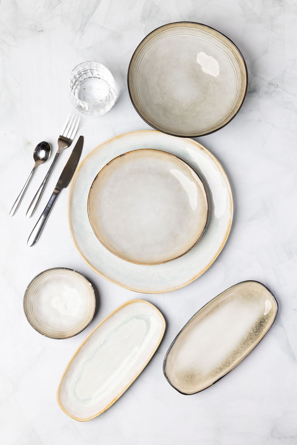 Minimalist place setting with cream colored ceramic plates and bowls on marble surface.