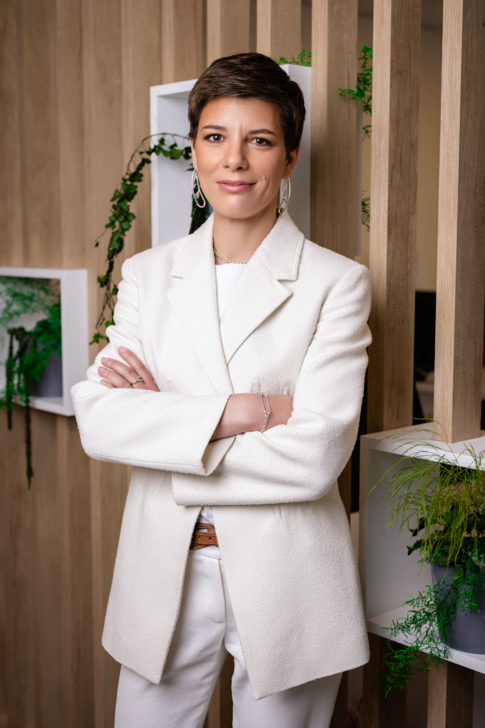 Professional poses confidently against wooden slat wall wearing crisp white blazer.