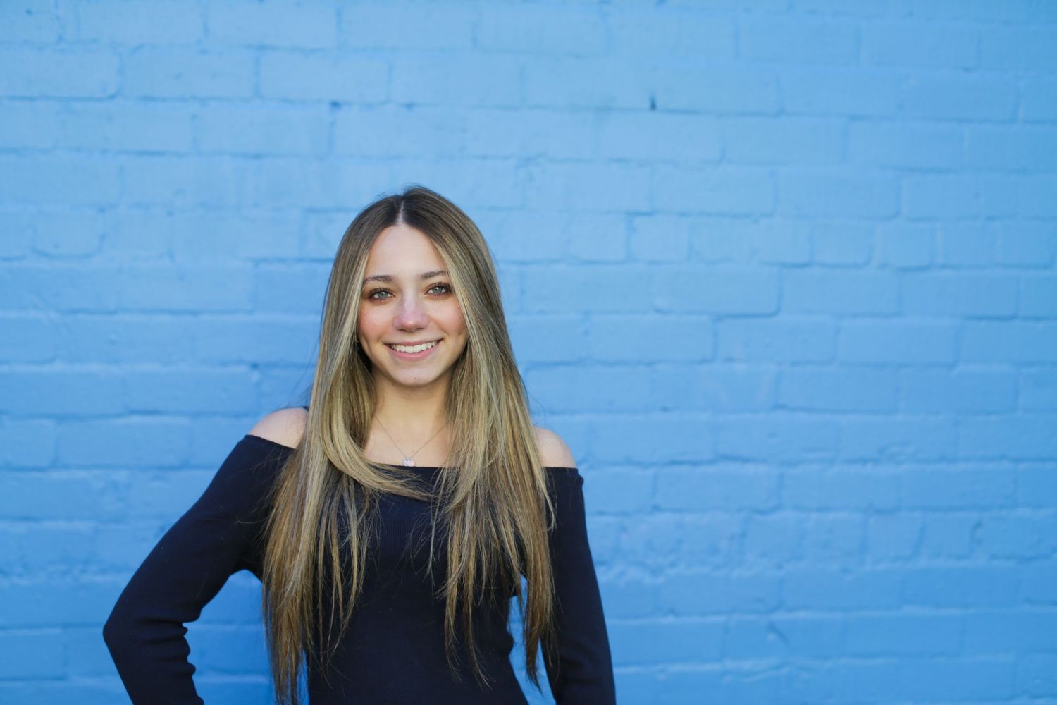 Senior portrait of a young woman smiling with downtown Tucson’s urban skyline and colorful murals in the background.