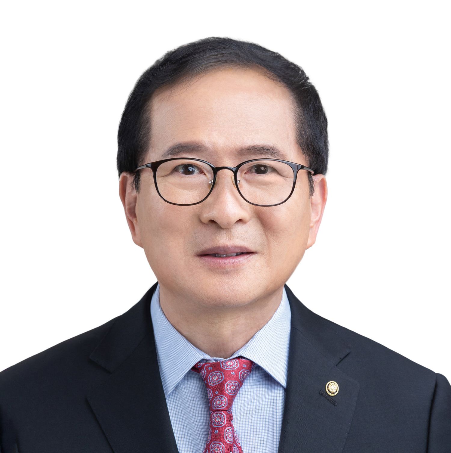 Professional wearing a dark business suit and round glasses poses in front of a clean white background.