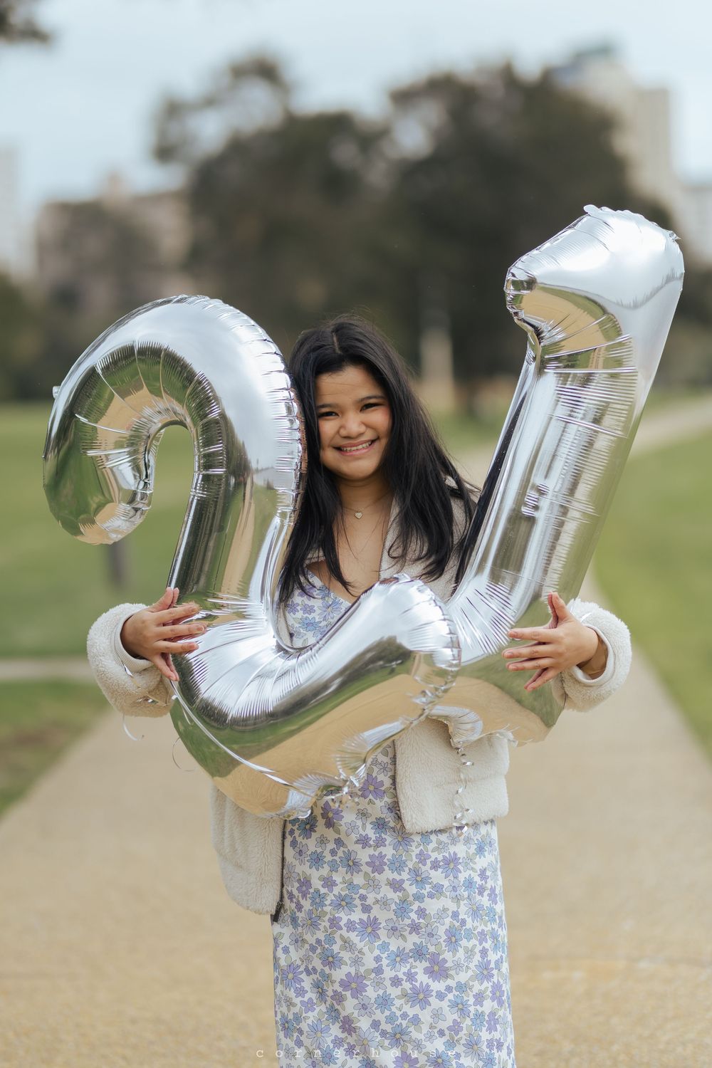Someone holds shiny silver letter balloons spelling JOY outdoors on a sunny day against a blurred natural background.