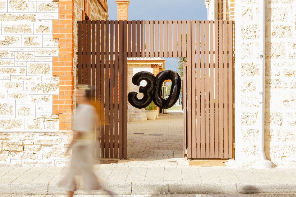 Iron gates with number 30 on a rustic stone building facade in a Mediterranean courtyard setting.