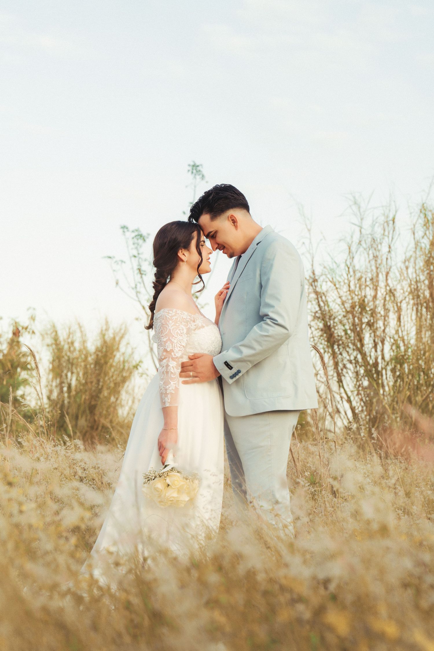 Wedding couple shares a tender embrace amidst golden wild grass.