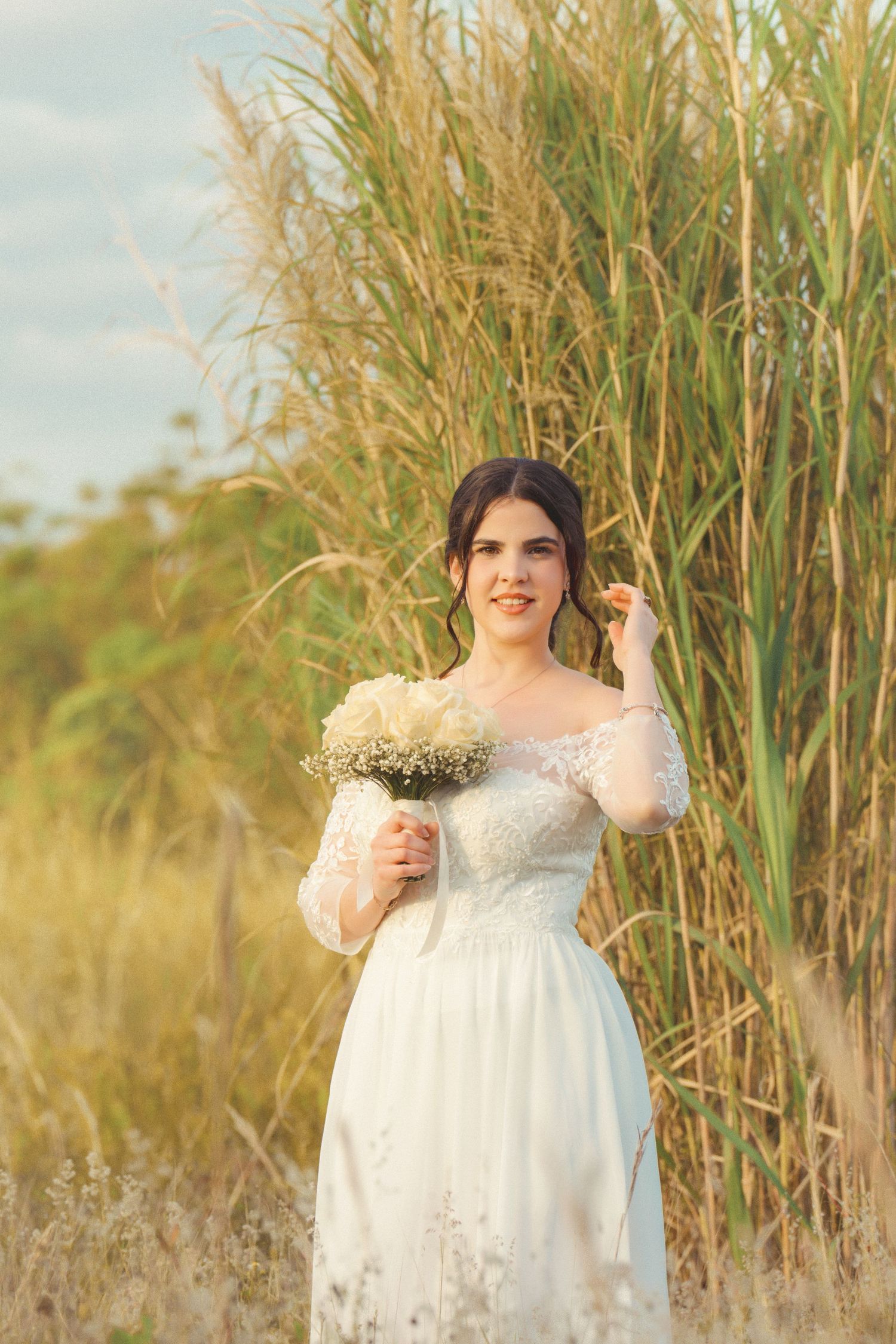 Bride holds a delicate bouquet while standing in a field of wild grass.