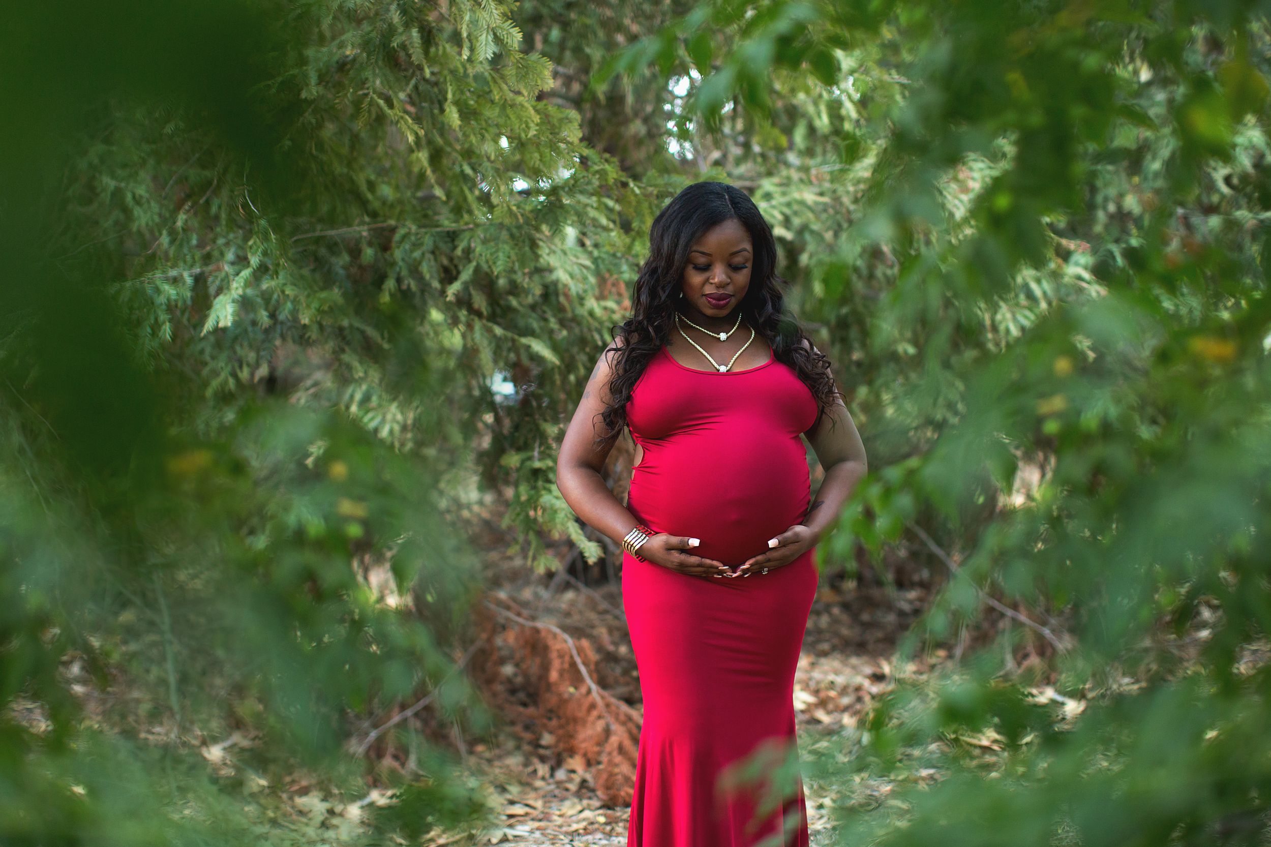A maternity photoshoot in a lush green garden setting with natural lighting.