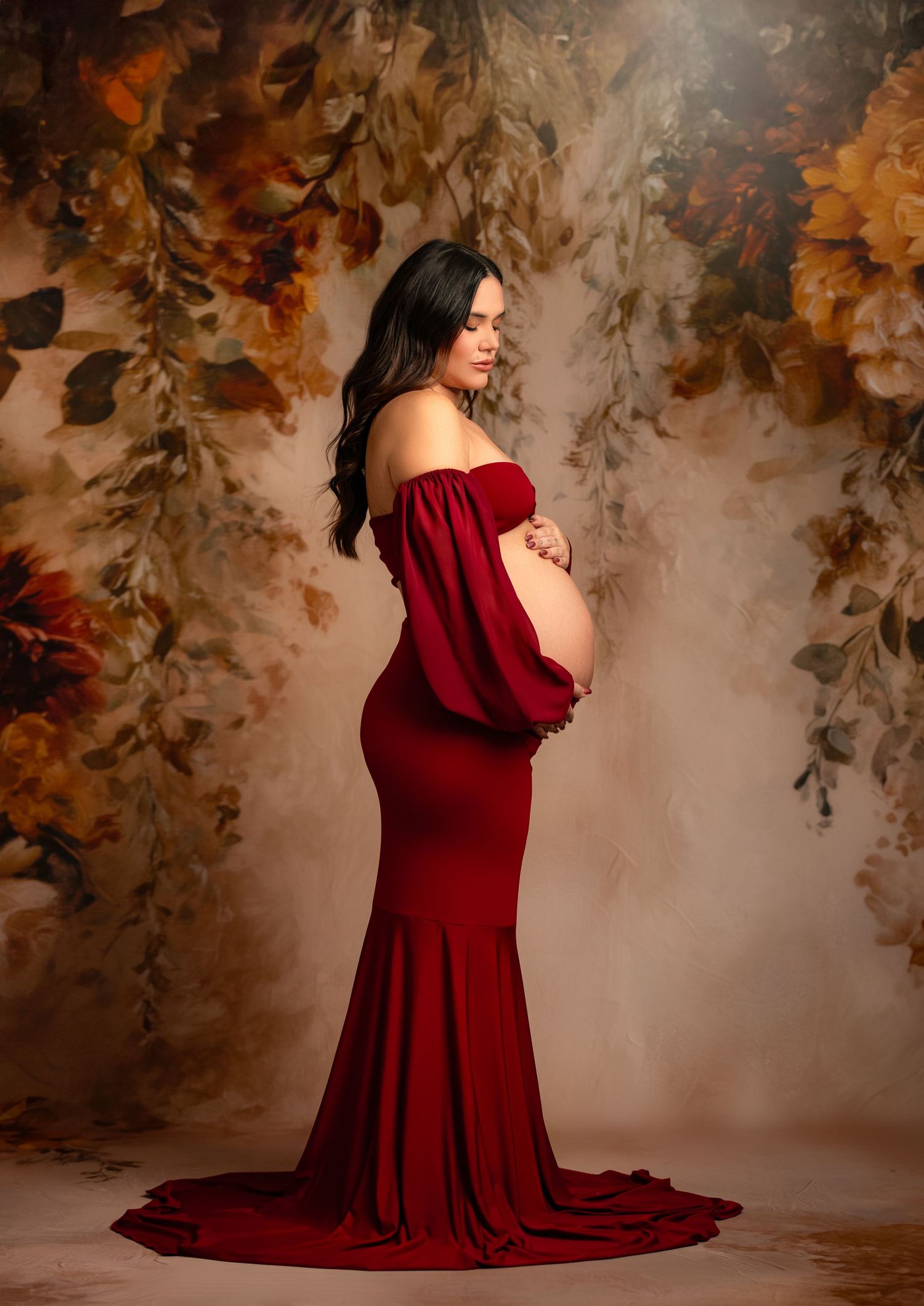 A person stands elegantly in a flowing red gown against a deep red background with classic wall paneling.